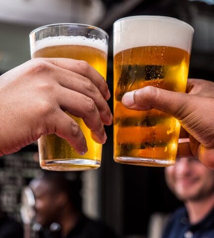 Close-up of two friends toasting with cold beer glasses at a lively bar, celebrating friendship and good times.