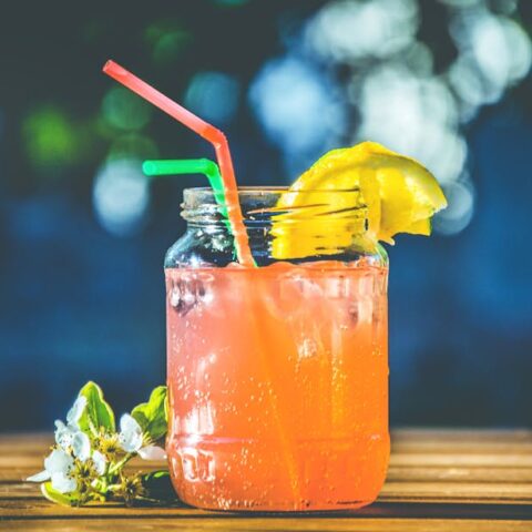 Refreshing summer citrus cocktail served in a mason jar with lemon slices and straws.
