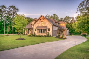 Elegant stone family home surrounded by trees, lush lawn, and vibrant garden.